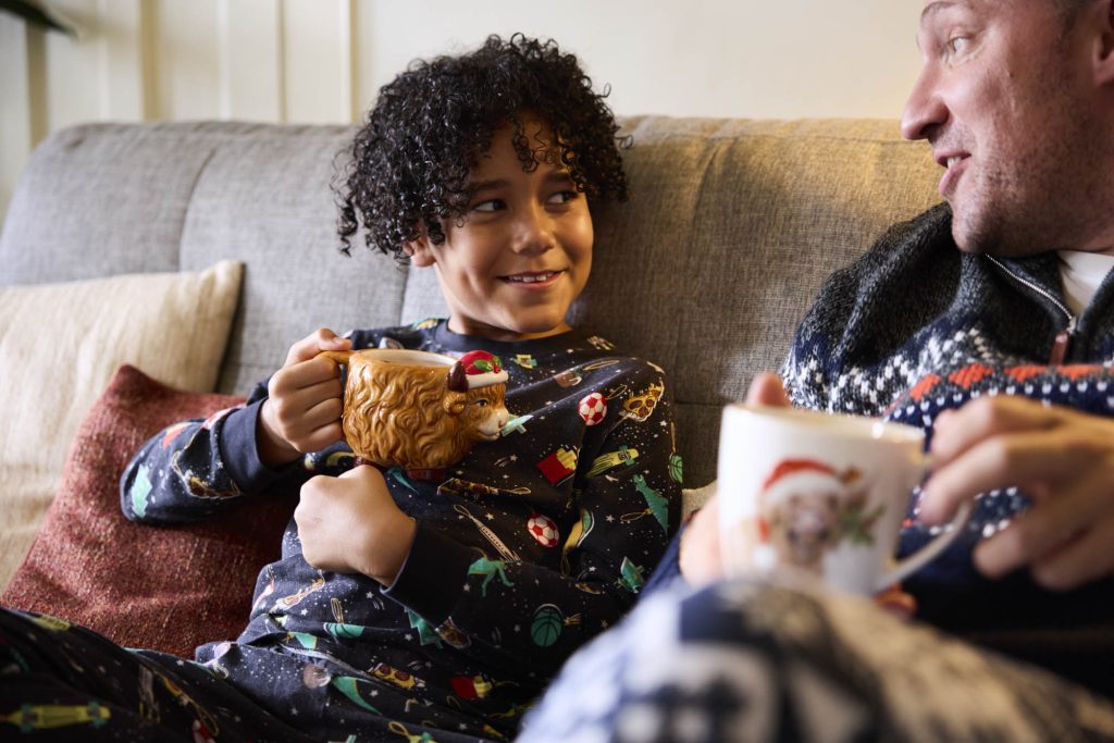 Child in Christmas pyjamas relaxing on a sofa holding a novelty Christmas mug