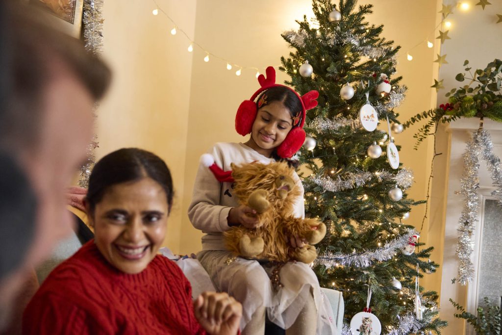 Woman smiling with a child holding a Christmas teddy bear beside a decorated tree